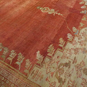 Distressed, low-pile rug featuring a vibrant brick red field next to a light beige floral border.