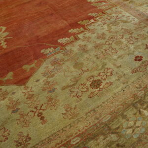 Faded rug showing a distressed red field and a wide khaki border with repeating floral motifs.
