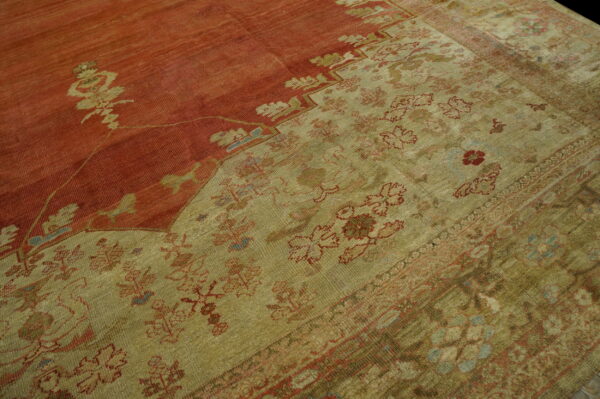 Faded rug showing a distressed red field and a wide khaki border with repeating floral motifs.