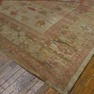Low-pile rug in khaki and faded red traditional patterns covers worn diagonal wood planks.
