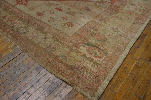 Low-pile rug in khaki and faded red traditional patterns covers worn diagonal wood planks.