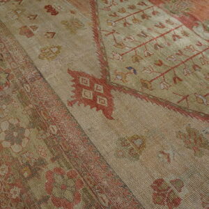 Low-pile rug with striated beige texture and faded red traditional patterns on wood flooring.
