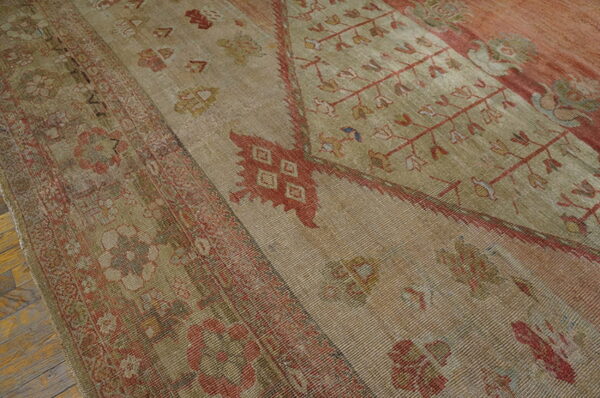 Low-pile rug with striated beige texture and faded red traditional patterns on wood flooring.