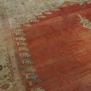 Close-up of a low-pile rug with a faded reddish-orange field and a wide beige border featuring floral motifs.