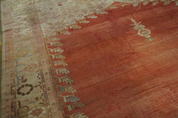 Close-up of a low-pile rug with a faded reddish-orange field and a wide beige border featuring floral motifs.