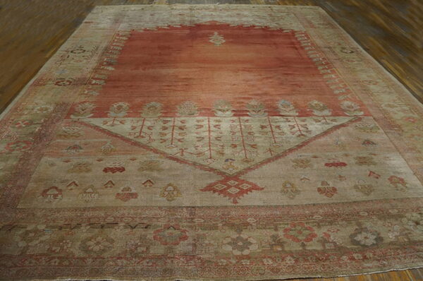 Rust and tan patterned rug with low pile and abrash fading sits on dark brown hardwood floors.
