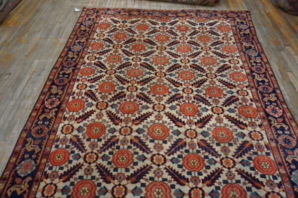 Ivory rug with repeating terracotta floral medallions and navy blue geometric motifs displayed on wood flooring.