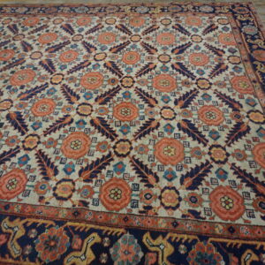 A large traditional rug with coral and navy botanical patterns on a cream field rests on distressed wood planks.