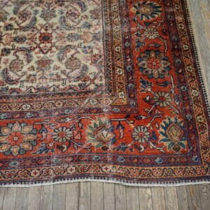 Cream and red traditional floral rug with a contrasting border rests on distressed gray hardwood floors.