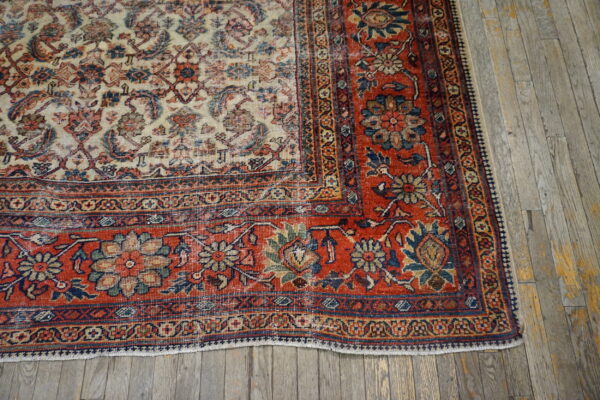 Cream and red traditional floral rug with a contrasting border rests on distressed gray hardwood floors.