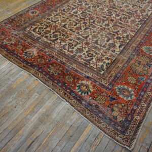 Ornate rug with a cream field and rust red border featuring detailed floral patterns on distressed wood flooring.