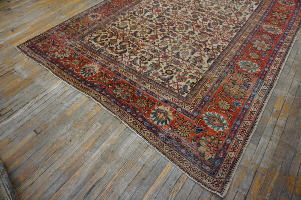 Ornate rug with a cream field and rust red border featuring detailed floral patterns on distressed wood flooring.