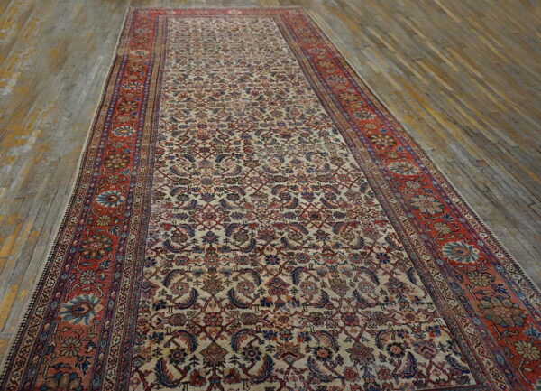 Detailed runner rug with a cream floral pattern and rust border lying on rustic wood flooring.