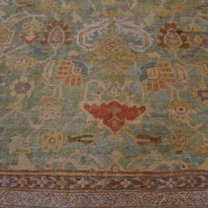 Muted green and tan low-pile rug with complex traditional designs featuring accents of red, gold, and blue.