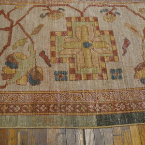 Muted beige, rust, and green traditional patterned rug with a worn texture rests on wood plank flooring.