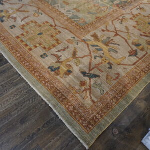Low-pile traditional rug corner featuring beige, rust, gold, and green patterns, resting on dark wood planks.