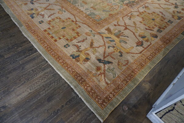 Low-pile traditional rug corner featuring beige, rust, gold, and green patterns, resting on dark wood planks.