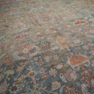 Low-pile rug with a complex floral pattern in distressed teal, rust, and beige tones.