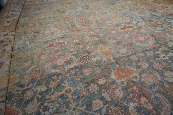 Low-pile rug with a complex floral pattern in distressed teal, rust, and beige tones.