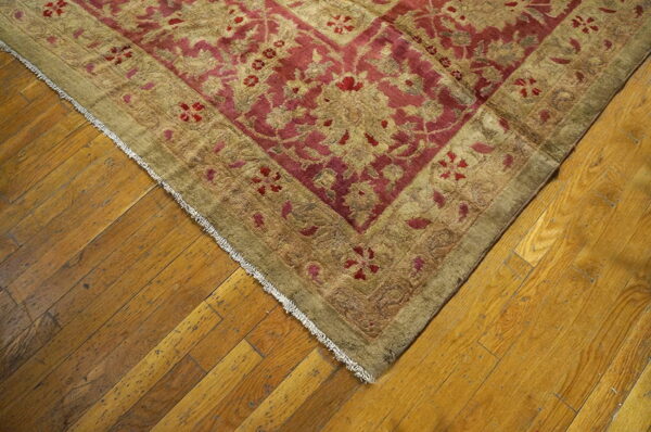 Red and khaki traditional rug with a floral pattern rests on diagonal distressed hardwood flooring.