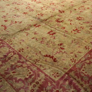 Low pile rug in faded khaki and deep red with a wide decorative floral border design.