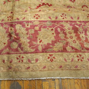 Close-up of a traditional rug featuring beige and magenta floral borders lying on a hardwood floor.