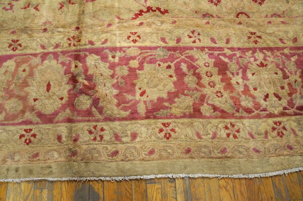 Close-up of a traditional rug featuring beige and magenta floral borders lying on a hardwood floor.