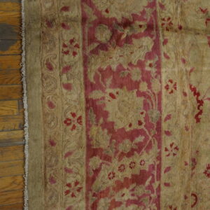 Khaki and deep pink traditional rug with detailed floral borders rests on shiny wood flooring.