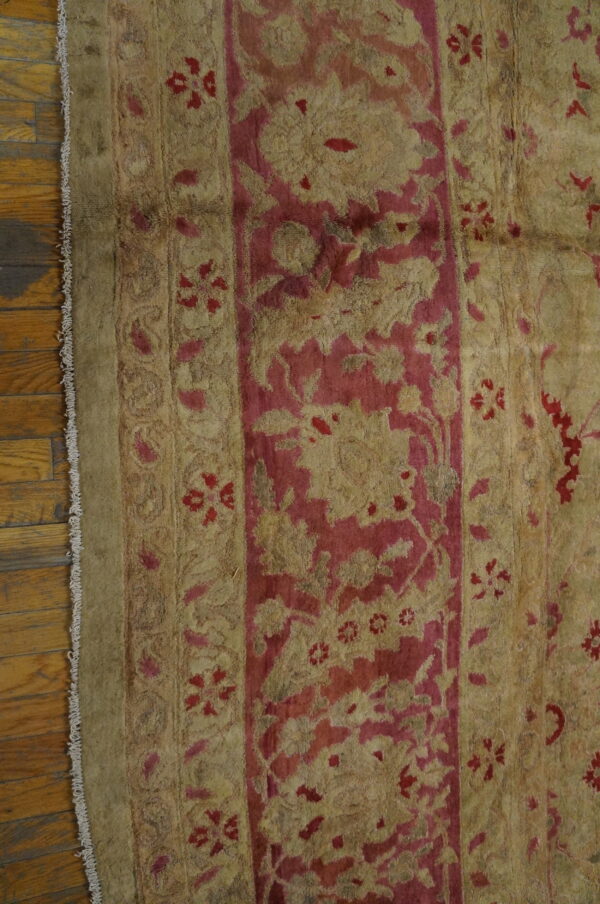 Khaki and deep pink traditional rug with detailed floral borders rests on shiny wood flooring.