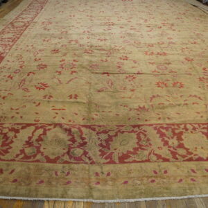 Large faded rug featuring deep red floral patterns on a gold and olive green field on a wood floor.