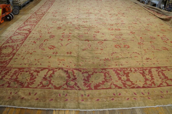 Large faded rug featuring deep red floral patterns on a gold and olive green field on a wood floor.