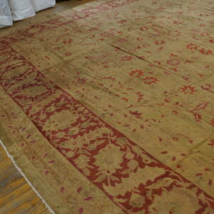 Low-pile gold rug with red floral patterns and a wide red border, displayed on distressed wood planks.
