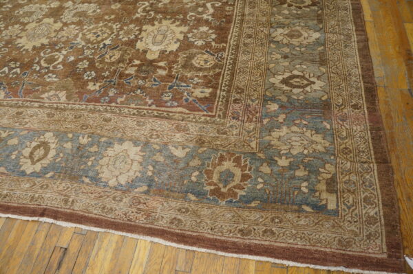 Low-pile rug with central brown field and faded blue border, resting on wooden plank flooring.