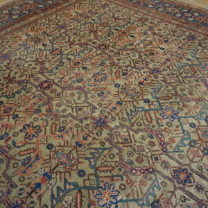 Geometric area rug in muted green, blue, red, and pink colors lies on wide wooden floorboards.