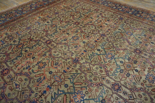 Geometric area rug in muted green, blue, red, and pink colors lies on wide wooden floorboards.