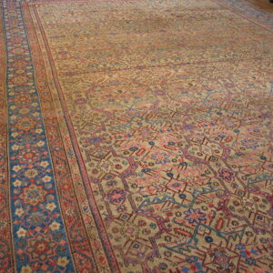 Khaki field rug with dense pink and blue geometric designs and a broad patterned blue side border.