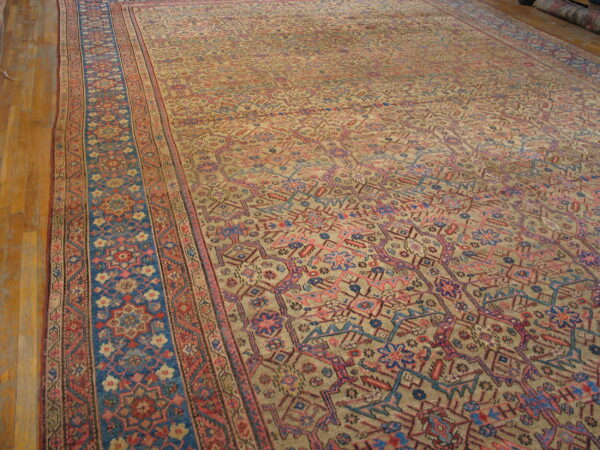 Khaki field rug with dense pink and blue geometric designs and a broad patterned blue side border.