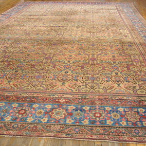 Oversized beige rug with detailed multicolored geometric designs and broad blue borders on plank wood.