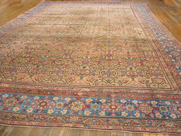 Oversized beige rug with detailed multicolored geometric designs and broad blue borders on plank wood.