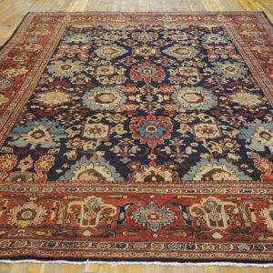 Navy blue traditional rug with a detailed multicolored floral pattern and wide rust red borders on wood flooring.