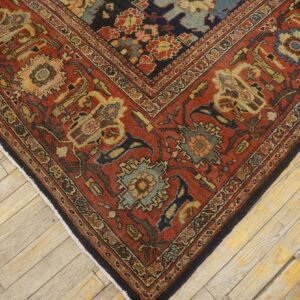 Close-up of a detailed red, navy, and gold patterned rug corner on light wooden planks.