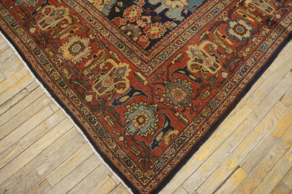 Close-up of a detailed red, navy, and gold patterned rug corner on light wooden planks.