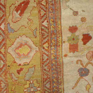 A patterned border separates a textured gold rug field from an adjacent beige flat weave with floral motifs.