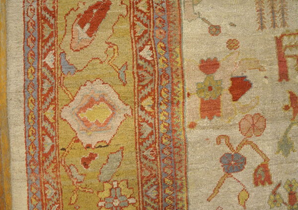 A patterned border separates a textured gold rug field from an adjacent beige flat weave with floral motifs.