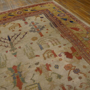 A low-pile beige rug with stylized red and blue botanical patterns is centered by a wide olive border on wood flooring.
