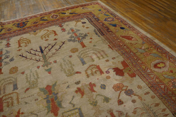 A low-pile beige rug with stylized red and blue botanical patterns is centered by a wide olive border on wood flooring.