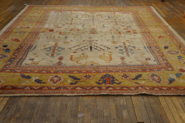 Cream rug with scattered tribal motifs and a wide mustard yellow border on distressed wood floors.