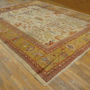 Low-pile rug with light field and wide mustard yellow border featuring stylized folk patterns on worn wooden flooring.