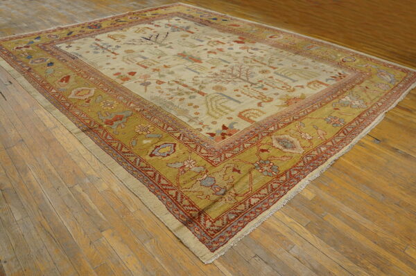 Low-pile rug with light field and wide mustard yellow border featuring stylized folk patterns on worn wooden flooring.