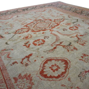 Close-up view of a textured rug corner showing a beige field, rust patterns, and multicolored decorative borders.